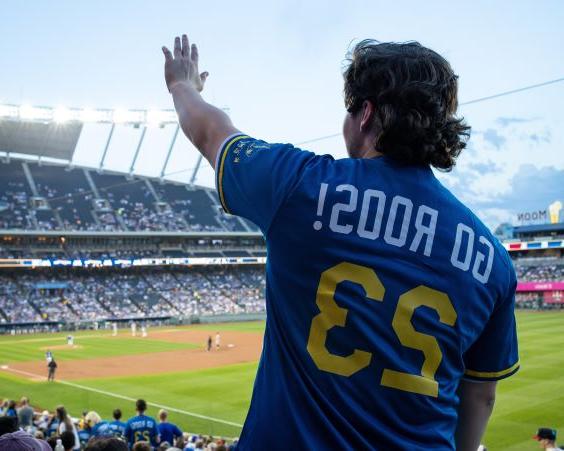 UMKC student shown from the back wearing a Go Roos jersey and waving to the other side of Kauffman Stadium where the Royals play